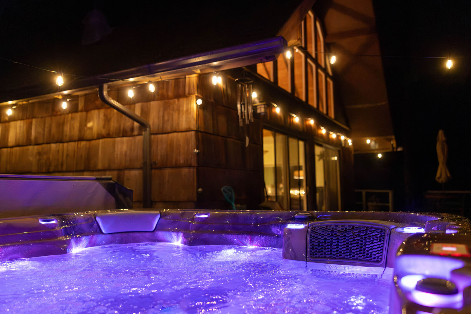 Hot tub glowing at night under string lights
